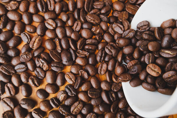 full of coffee beans spilling out white ceramic cup on brown wooden background