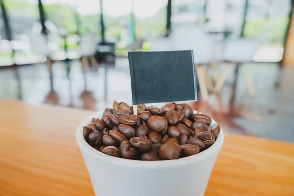 Chicco di caffè in tazza di ceramica bianca e bandiera nera con sfondo in legno marrone — Foto Stock