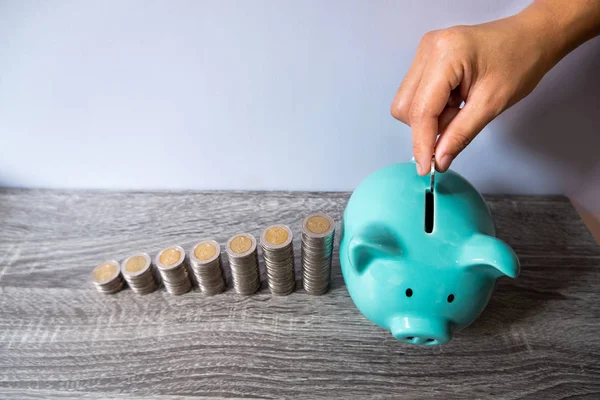 woman hand putting coin into blue piggy bank with coins growth bar graph, step up growing business to success and saving for retirement concept