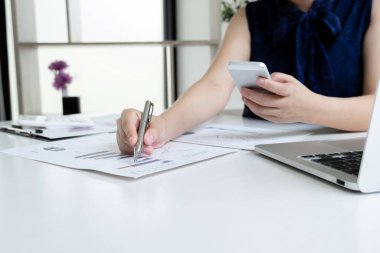 Ofisteki kız masada oturuyor ve ofiste sonuçları gösteren telefon hesaplama grafiğini kullanıyor..