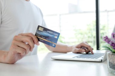 Kredi kartı tutan ve online alışveriş için dizüstü bilgisayar kullanan ve ödemeleri internet üzerinden yapan genç adamlar..