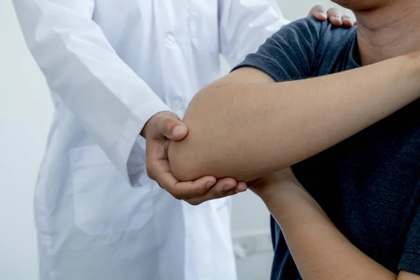 Kadın fizyoterapistler, dirsek yaralanması olan erkek hastalara rehabilitasyon merkezlerindeki hastaları muayene etmede yardımcı oluyorlar. Fizyoterapi kavramları.