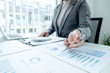 İş kadını, iş yatırımları için mali düzenlemeleri gösteren ve analiz eden finansal grafikler hesaplıyor.
