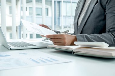İş kadını, iş yatırımları için mali düzenlemeleri gösteren ve analiz eden finansal grafikler hesaplıyor.