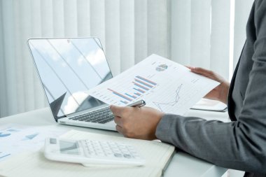 İş kadını, iş yatırımları için mali düzenlemeleri gösteren ve analiz eden finansal grafikler hesaplıyor.