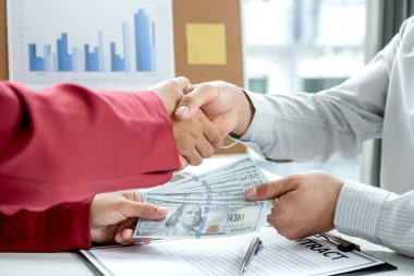 İş adamlarının el sıkışırken çekilmiş bir fotoğrafı ve şirketteki yolsuzluğa rüşvet verme sözleşmesi. Rüşvet ve yolsuzluk kavramı.