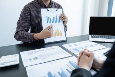 Sonuçları gösteren çizelge ve grafikleri tartışan iki iş lideri ofiste büyük bir başarı için yeni bir strateji başlatmayı planlıyorlar..