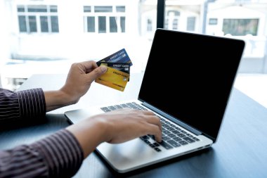 İş adamının elinde bir kredi kartı var ve ofisteki online alışveriş ve internet ödemeleri için dizüstü bilgisayar kullanıyor..