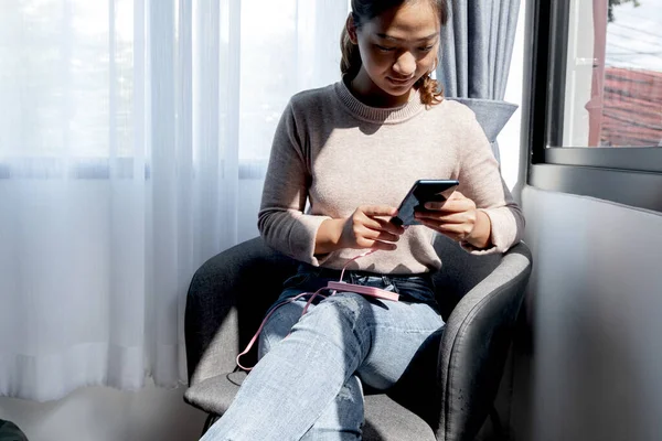 The hand of a young woman holding a smartphone and a modern spare battery charger Place the lap to charge the smartphone with a spare battery charger and play on a chair in the room.