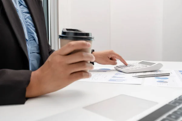 The hands of a male businesswoman use the calculator are analyzing and calculating the annual income and expenses in a financial graph that shows results To summarize balances overall in office.