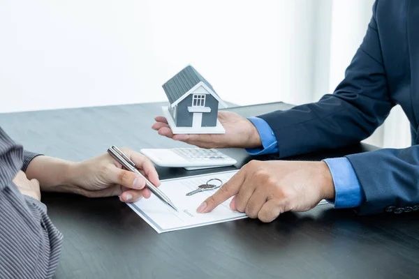 A real estate agent with a home model is talking to clients about renting a house and buying home insurance and contracting the contract after the formal negotiation is completed.