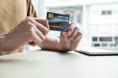 İş adamının elinde bir kredi kartı var ve ofisteki online alışveriş ve internet ödemeleri için dizüstü bilgisayar kullanıyor..