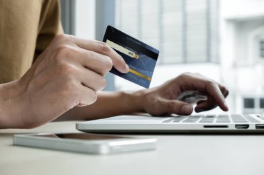 İş adamının elinde bir kredi kartı var ve ofisteki online alışveriş ve internet ödemeleri için dizüstü bilgisayar kullanıyor..