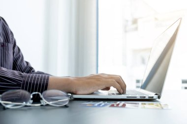 İş adamının elinde bir kredi kartı var ve ofisteki online alışveriş ve internet ödemeleri için dizüstü bilgisayar kullanıyor..