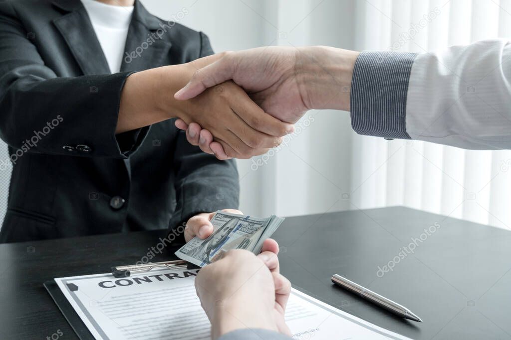 photo of Businessmen shakes hands and dollar note, sign a contract to bribe corruption in the company. The concept of bribery and corruption.