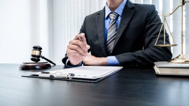 Profesyonel erkek avukatlar bir hukuk bürosunda çalışır. Teraziler, adalet terazileri, yargıç tokmağı ve dava belgeleri vardır. Hukuk ve adalet kavramları.