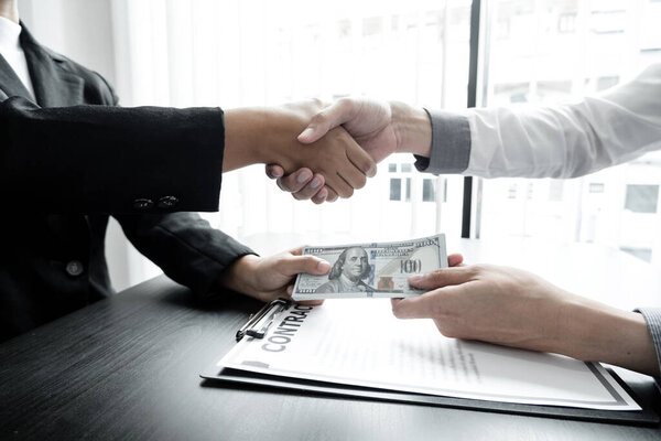 фото бизнесменов, пожимающих руки и долларовую банкноту, подписывающих контракт на подкуп коррупции в компании. Концепция взяточничества и коррупции.