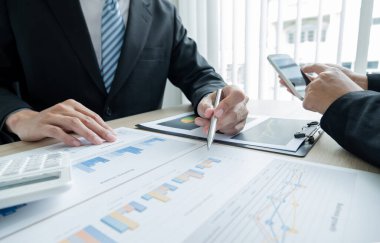 İki iş lideri çizelgeler, finansal grafikler hakkında konuşuyor. Sonuçları gösteren planlama stratejilerini analiz ediyor ve hesaplıyor. Ticari başarı oluşturma süreçlerini de..