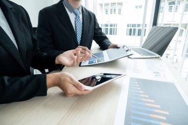 İki iş lideri çizelgeler, finansal grafikler hakkında konuşuyor. Sonuçları gösteren planlama stratejilerini analiz ediyor ve hesaplıyor. Ticari başarı oluşturma süreçlerini de..