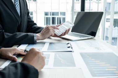 İki iş lideri çizelgeler, finansal grafikler hakkında konuşuyor. Sonuçları gösteren planlama stratejilerini analiz ediyor ve hesaplıyor. Ticari başarı oluşturma süreçlerini de..