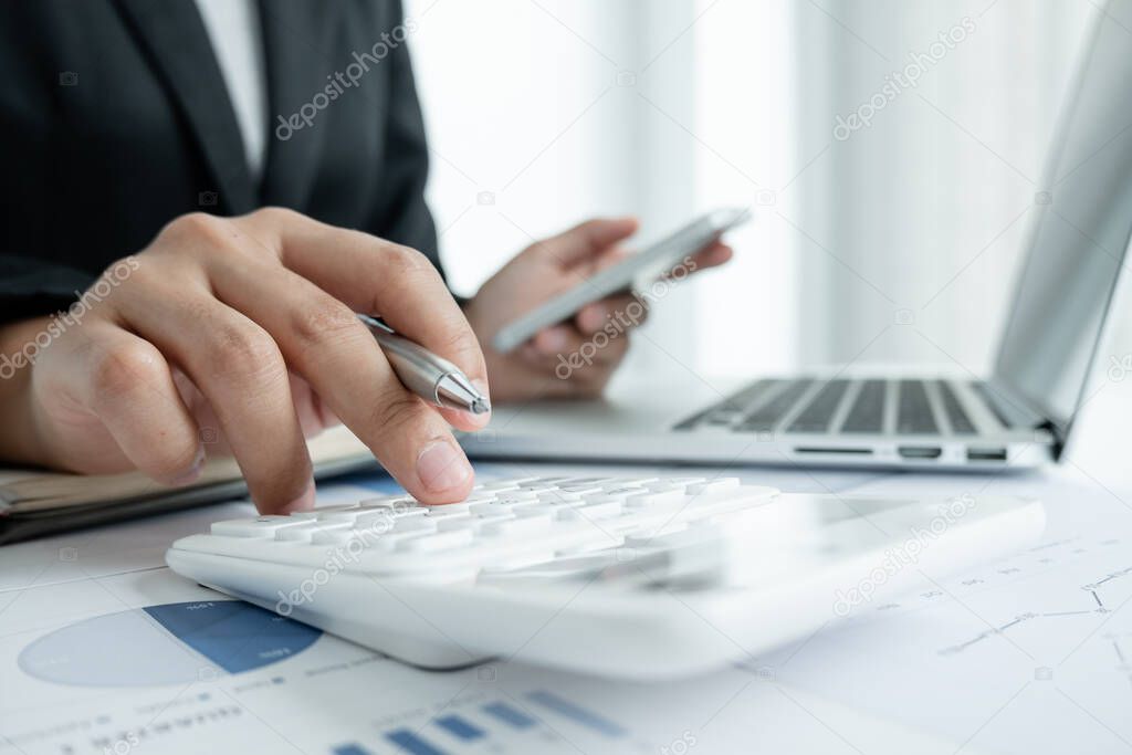 The hands of a male businesswoman use the calculator are analyzing and calculating the annual income and expenses in a financial graph that shows results To summarize balances overall in office.