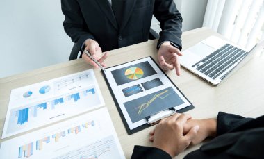 İki iş lideri çizelgeler, finansal grafikler hakkında konuşuyor. Sonuçları gösteren planlama stratejilerini analiz ediyor ve hesaplıyor. Ticari başarı oluşturma süreçlerini de..