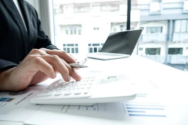 The hands of a male businesswoman use the calculator are analyzing and calculating the annual income and expenses in a financial graph that shows results To summarize balances overall in office.