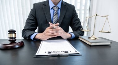 Profesyonel erkek avukatlar bir hukuk bürosunda çalışır. Teraziler, adalet terazileri, yargıç tokmağı ve dava belgeleri vardır. Hukuk ve adalet kavramları.