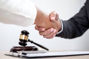 Hukuk bürosunda çalışan profesyonel erkek avukatların tokalaşması için teraziler, adalet terazileri, yargıç tokmağı ve dava belgeleri var. Hukuk ve adalet kavramları.