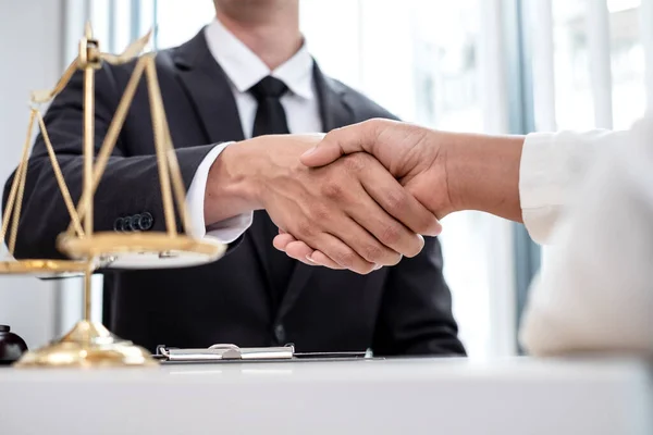 Hukuk bürosunda çalışan profesyonel erkek avukatların tokalaşması için teraziler, adalet terazileri, yargıç tokmağı ve dava belgeleri var. Hukuk ve adalet kavramları.