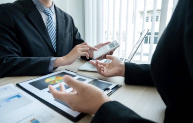 İki iş lideri çizelgeler, finansal grafikler hakkında konuşuyor. Sonuçları gösteren planlama stratejilerini analiz ediyor ve hesaplıyor. Ticari başarı oluşturma süreçlerini de..