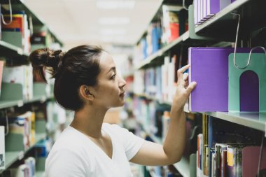Genç Asyalı kadınlar, kendilerini eğitim alanında geliştirmek ve araştırmak için üniversite kütüphanesindeki kitaplıklardan kitap arıyor ve okuyorlar..