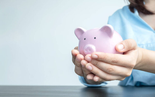 A woman's hand holds a piggy bank for saving into a growing business to succeed and save for retirement.