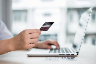 İş kadınının elinde bir kredi kartı var ve ofisteki online alışveriş ve internet ödemeleri için bir dizüstü bilgisayar kullanıyor..