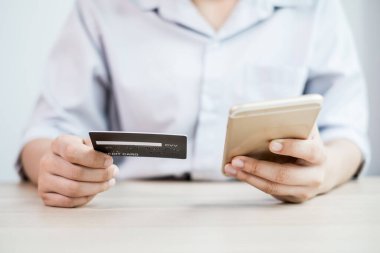 İş kadınının elinde bir kredi kartı var ve internet üzerinden alışveriş ve internet üzerinden ödeme yapmak için akıllı telefon kullanıyor..