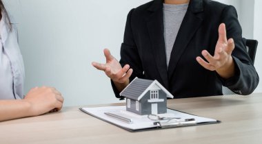 Ev modeli olan bir emlakçı ev kiralamak ve ev sigortası almak için müşterilerle konuşuyor. Ev kiralama ve sigorta konsepti.