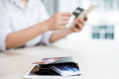 İş kadınının elinde bir kredi kartı var ve internet üzerinden alışveriş ve internet üzerinden ödeme yapmak için akıllı telefon kullanıyor..