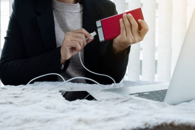 Akıllı bir telefon ve modern bir Power Bank şarj aleti tutan genç bir kadının eli. Masaya koy, akıllı telefonu yedek şarjla şarj et, oyun odasında oturan bir boyutta..