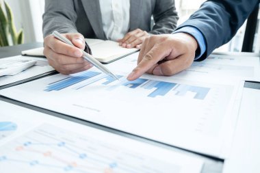 İki iş lideri çizelgeler, finansal grafikler hakkında konuşuyor. Sonuçları gösteren planlama stratejilerini analiz ediyor ve hesaplıyor. Ticari başarı oluşturma süreçlerini de..