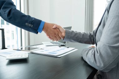 İki iş adamı el sıkışarak grafikler, finansal grafikler hakkında konuşuyor. Sonuçları gösteren planlama stratejileri analiz ediyor ve hesaplıyor. Ticari başarı oluşturma süreçleri..