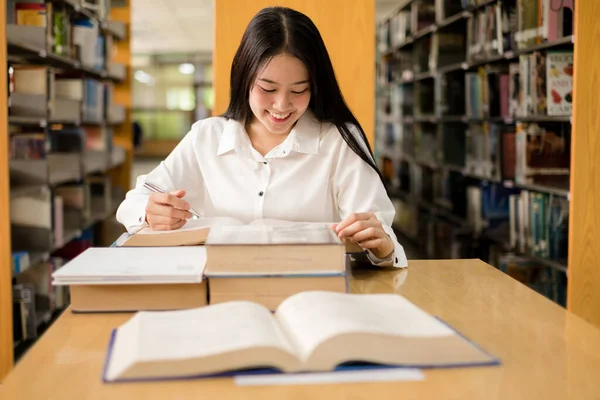 Young Asian women are searching for books and reading from the bookshelves in the college library to research and develop themselves in education.