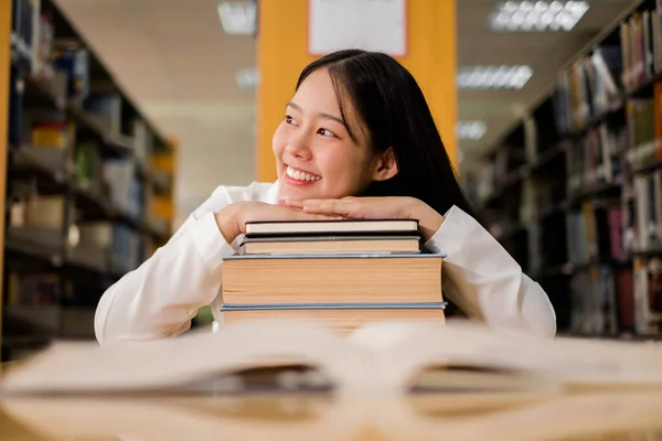 Genç Asyalı kadınlar, kendilerini eğitim alanında geliştirmek ve araştırmak için üniversite kütüphanesindeki kitaplıklardan kitap arıyor ve okuyorlar..
