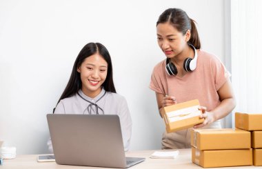 Asyalı kadın işi. Masasında bir sürü paket kutusu olan iki kişi mutlu bir online satış işi, bilgisayarınızı kullanın, müşterilerden emir alın, notlar alın ve posta yoluyla teslimat için düzenlemeler yapın..