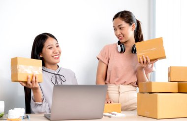 Asyalı kadın işi. Masasında bir sürü paket kutusu olan iki kişi mutlu bir online satış işi, bilgisayarınızı kullanın, müşterilerden emir alın, notlar alın ve posta yoluyla teslimat için düzenlemeler yapın..