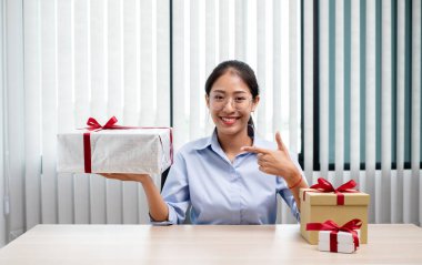 Asyalı kadın bir hediye kutusu tutuyor. Bayramlarda, Noel 'de, doğum günlerinde ya da Sevgililer Günü konseptinde sürpriz yapmaktan mutluluk duyuyor..