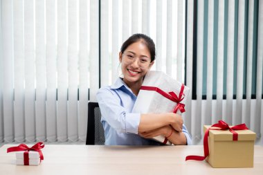 Asyalı kadın bir hediye kutusu tutuyor. Bayramlarda, Noel 'de, doğum günlerinde ya da Sevgililer Günü konseptinde sürpriz yapmaktan mutluluk duyuyor..