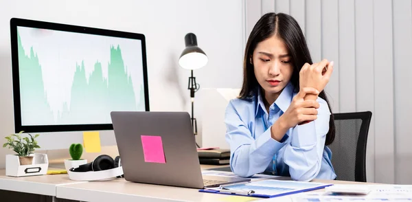 一位亚洲妇女在办公室工作时 正忙着用笔记本电脑加班 手腕酸痛 — 图库照片