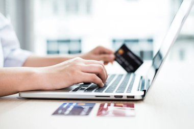 İş kadınının elinde bir kredi kartı var ve ofisteki online alışveriş ve internet ödemeleri için bir dizüstü bilgisayar kullanıyor..