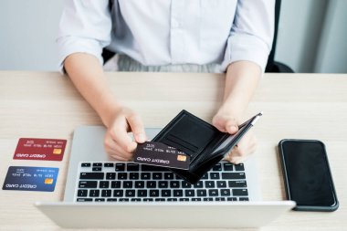 İş kadınının elinde bir kredi kartı var ve ofisteki online alışveriş ve internet ödemeleri için bir dizüstü bilgisayar kullanıyor..