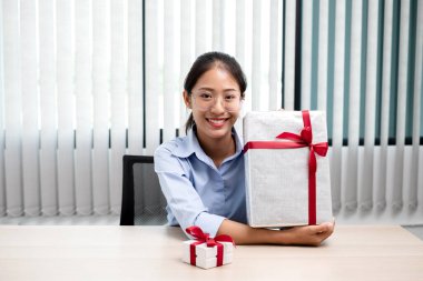 Asyalı kadın bir hediye kutusu tutuyor. Bayramlarda, Noel 'de, doğum günlerinde ya da Sevgililer Günü konseptinde sürpriz yapmaktan mutluluk duyuyor..